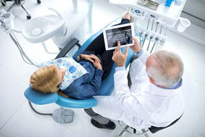 Zahnarzt an Behandlungsstuhl schaut auf Tablet mit Roentgenbild